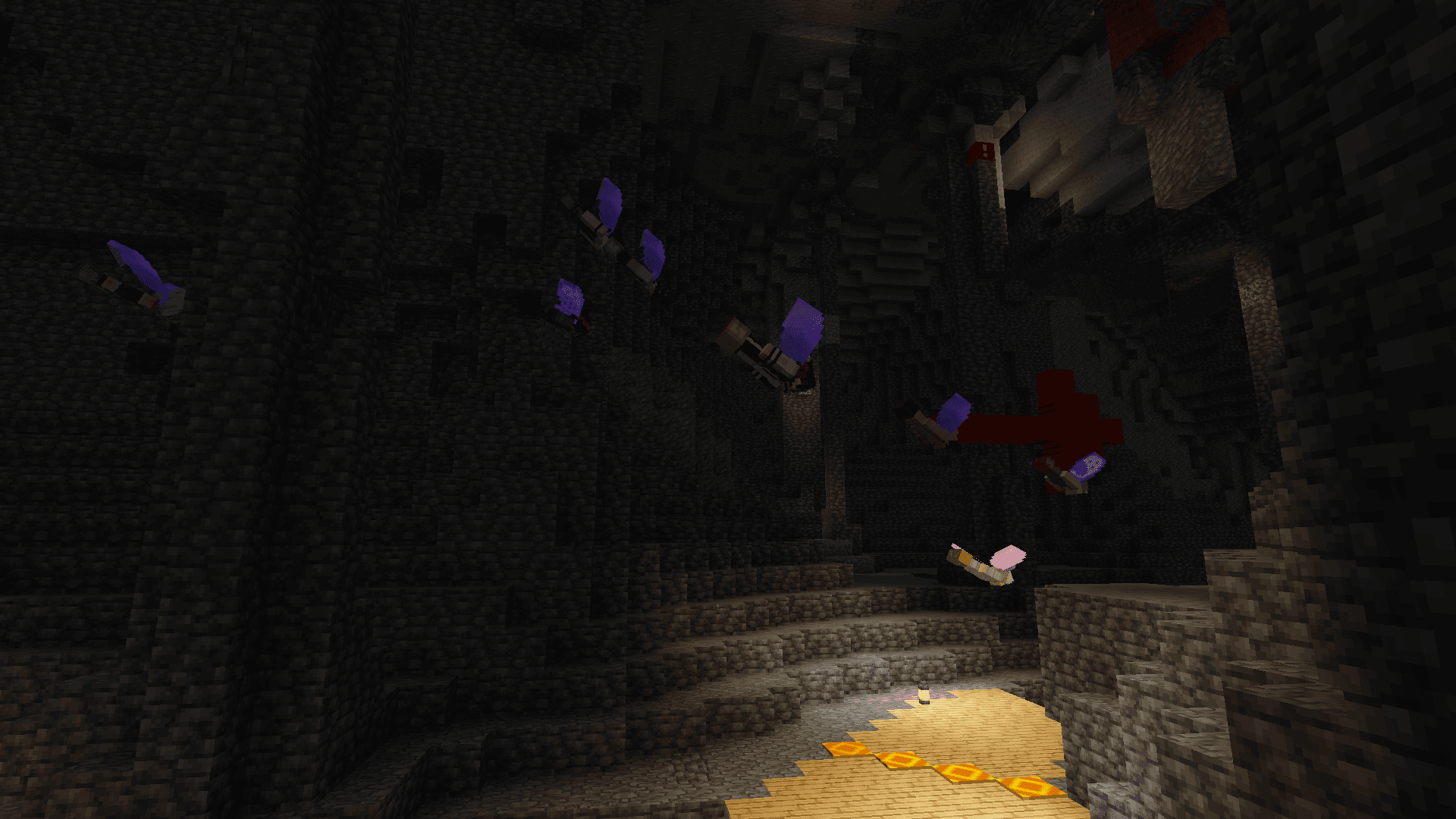 Players with elytra wings swooping through a darkened cave. There is a lamp on the floor of the cave providing light.